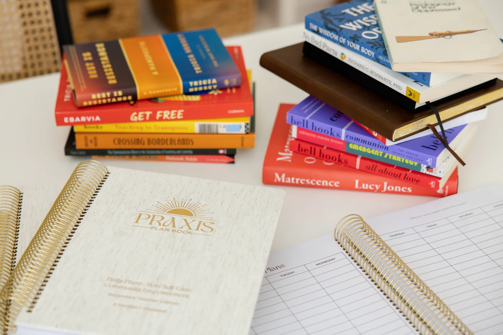Praxis Plan Books arranged on a writing table beside open planning pages and stacks of books