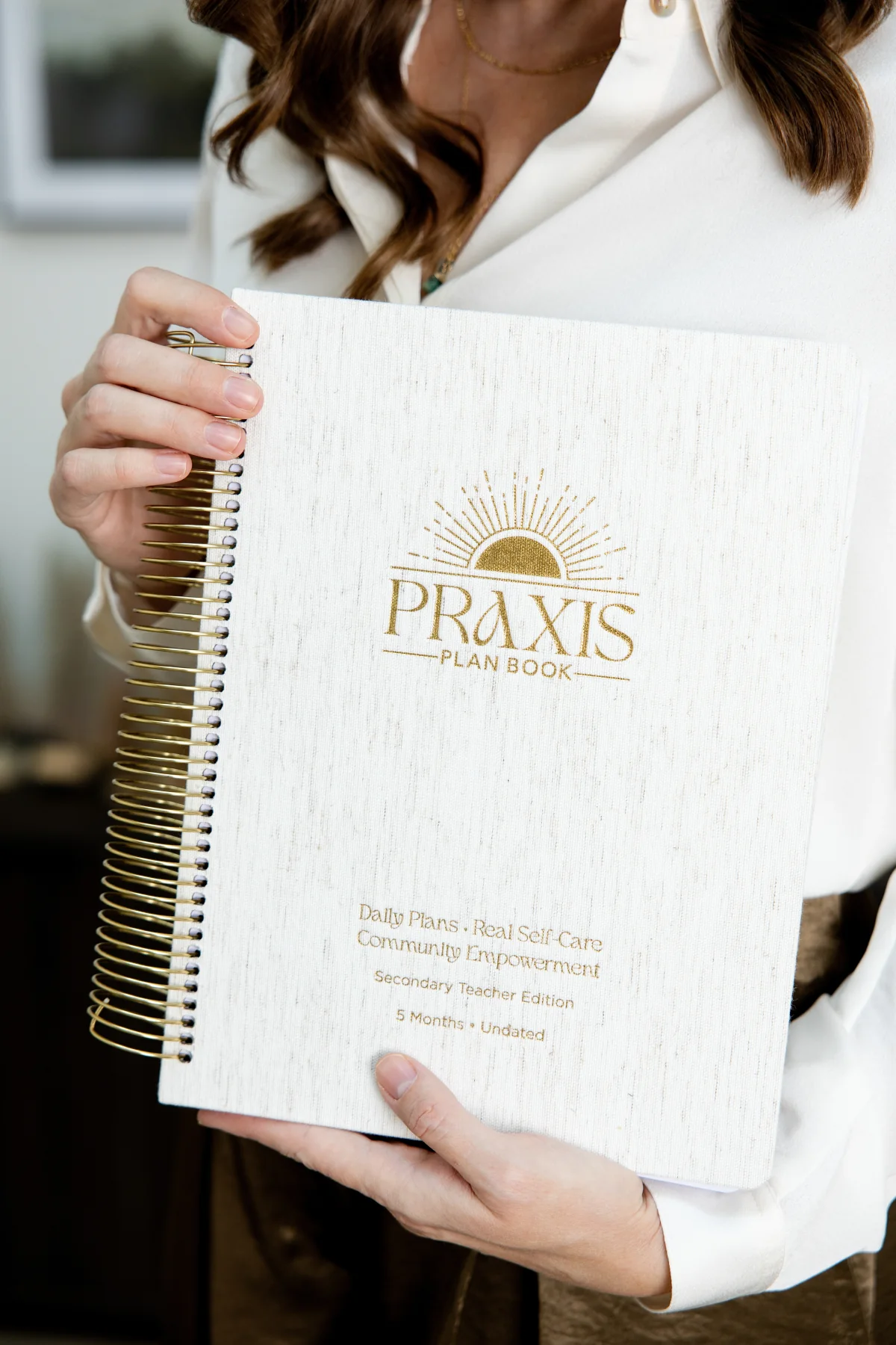 Close view of the Praxis Plan Book's cream flecked-linen cover, gold coil binding, and embroidered gold sunrise mark