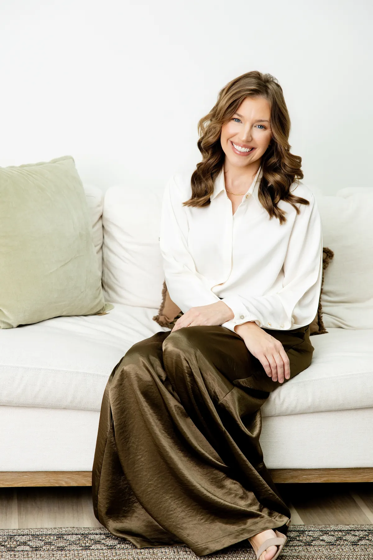 Sarah Bland seated on a cream sofa in a bright room, hands resting in her lap