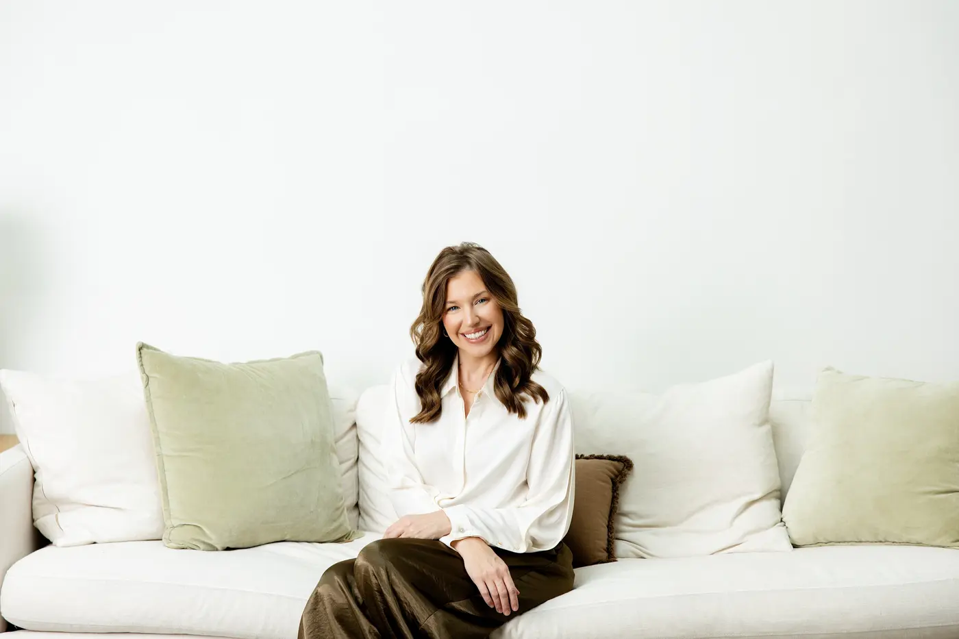 Sarah Bland, who taught secondary English before founding Enter Peace, sitting on a cream sofa between sage green cushions in a bright room